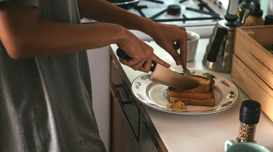 A home care worker cuts a grilled cheese sandwich in half.